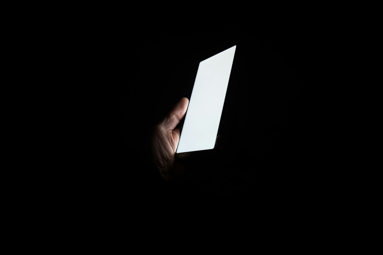 真っ暗な部屋で、白く光るスマートフォンを持つ手